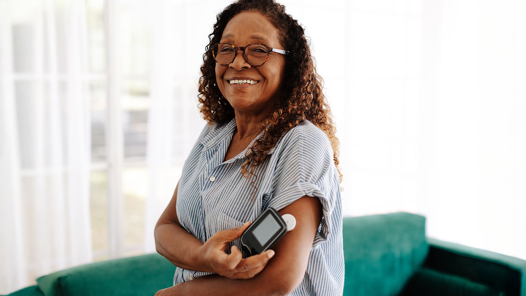 Nainen mittaa insuliinimittarilla arvoja käsivarrestaan ja katsoo kohti hymyillen.