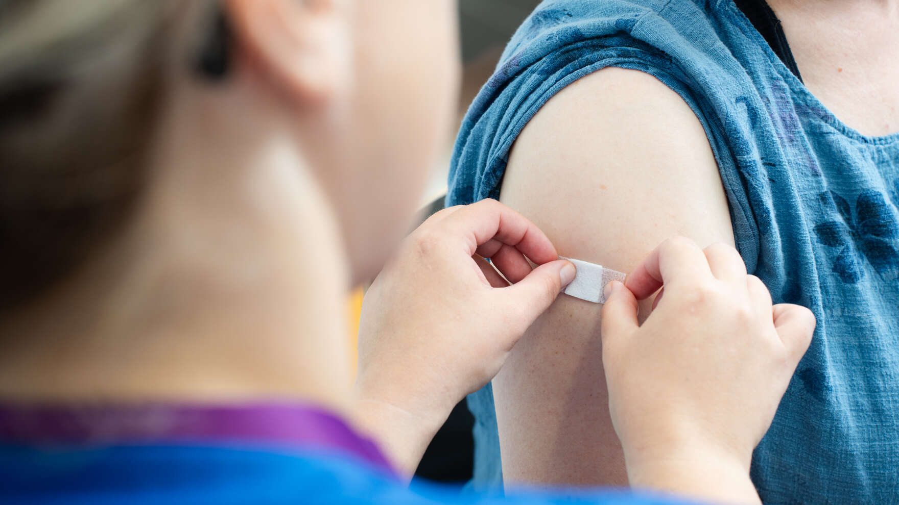 Lähikuva olkavarresta, johon hoitaja laittaa valkoisen laastarin rokotuksen jälkeen.