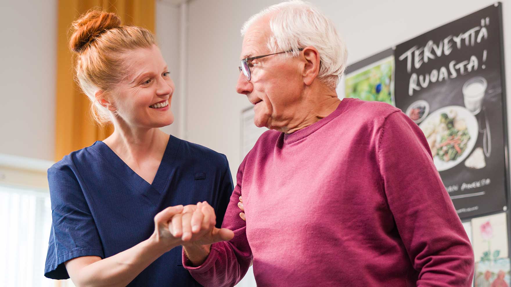 Sinipaitainen ammattilainen hymyilee ja pitää punapaitaista ikämiestä kädestä. Taustalla näkyy