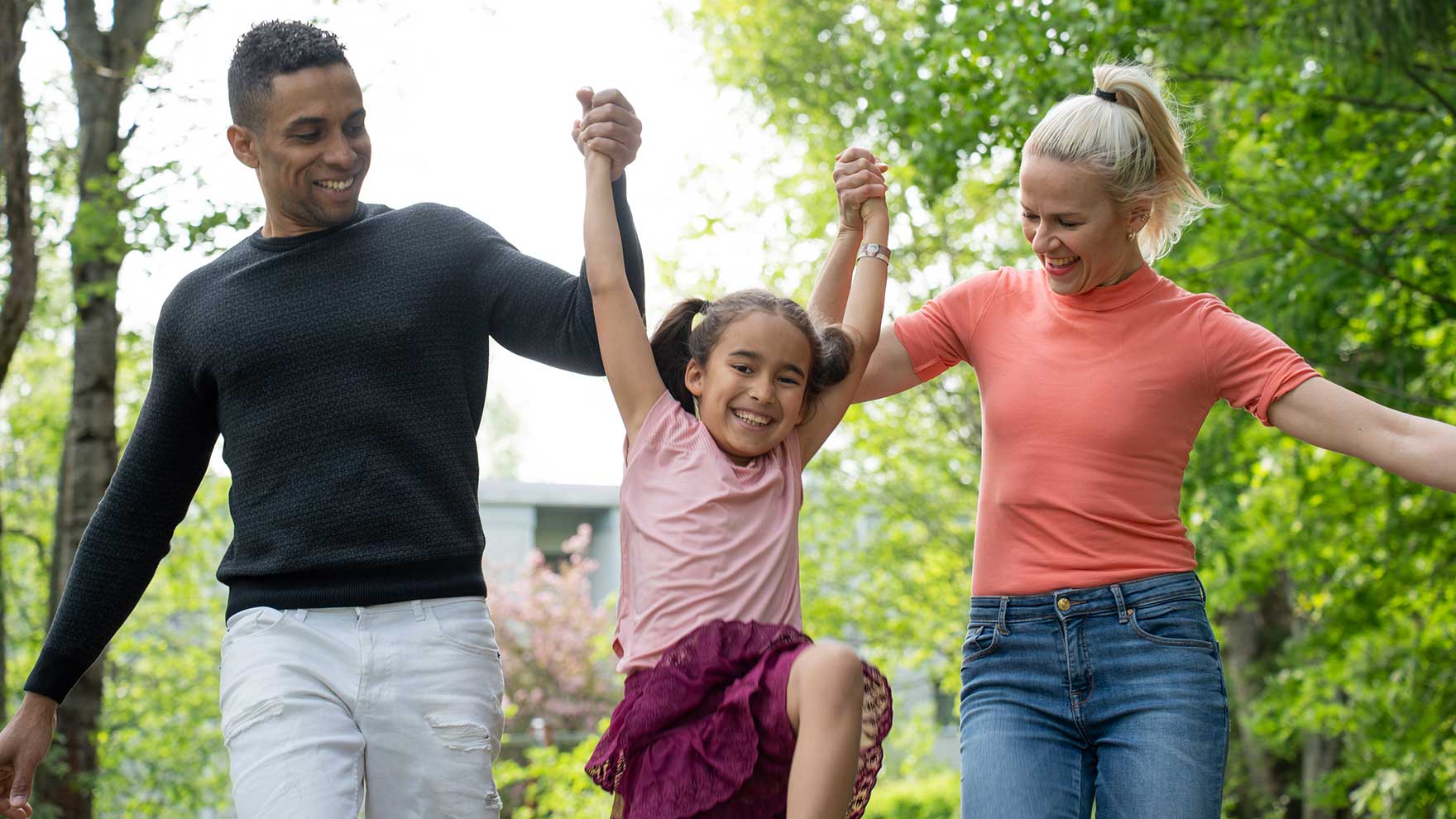 A girl jumps between her mother and father in a park.
