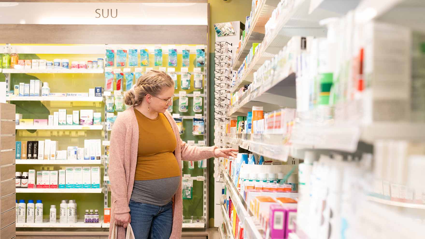 Odottava nainen tutkii apteekissa tuotehyllyjä. Taustalla on on suun terveyteen liittyviä tuotteita.