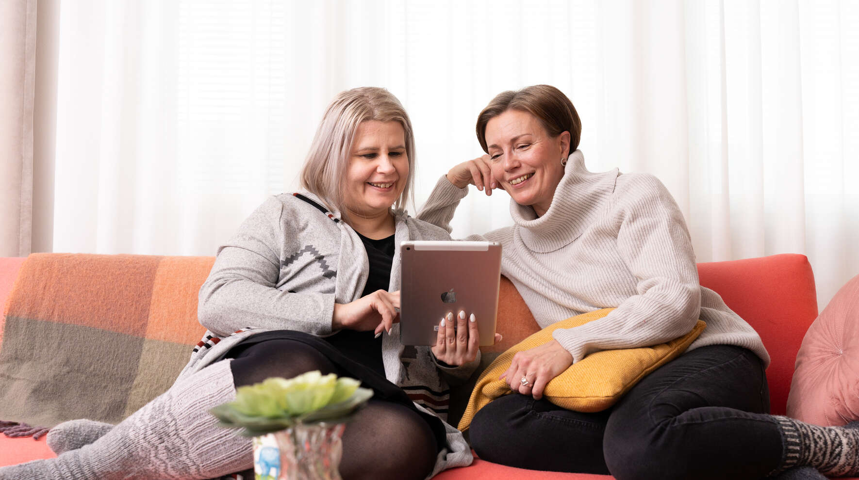Kaksi ihmistä katsovat sohvalla tablettia hymyillen.