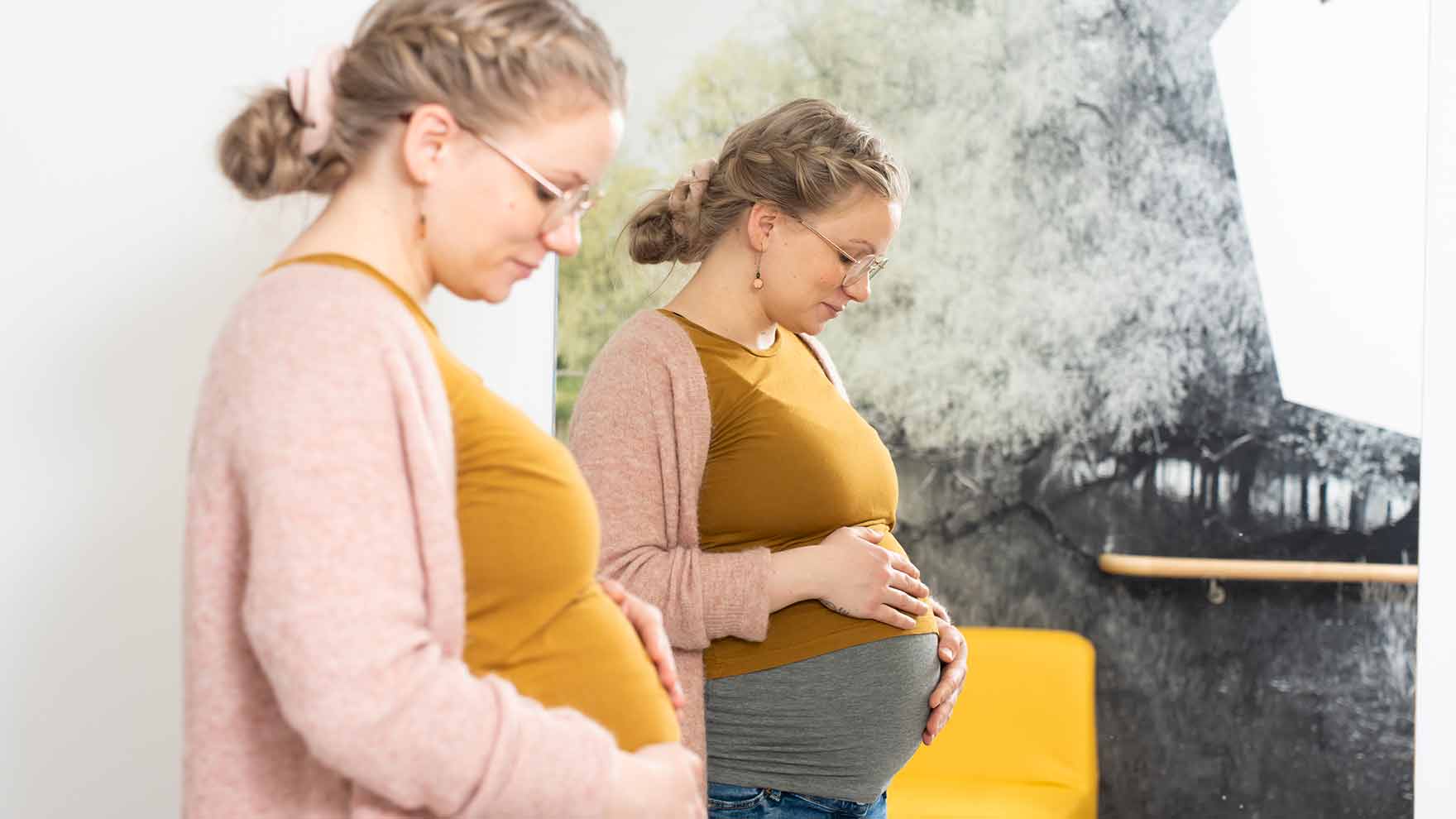 Odottava nainen on sivuttain kädet vatsalla. Hän näkyy tuplana peilikuvan kautta.