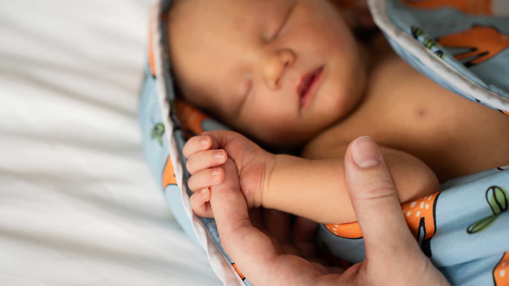 Vastasyntynyt viltin sisällä niin, että hänen sormensa pitävät kiinni aikuisen etusormesta.