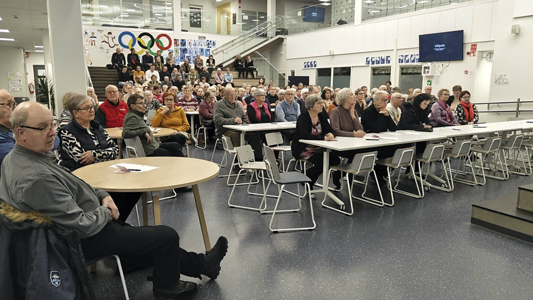 Paljon ihmisiä istumassa pöytien ääressä avoimessa salissa.