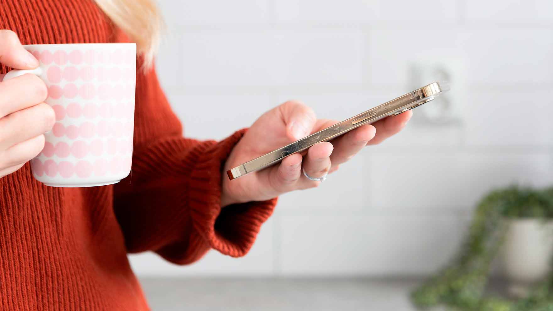 Lähikuva naisesta, jolla on toisessa kädessä kännykkä ja toisessa kahvikuppi.