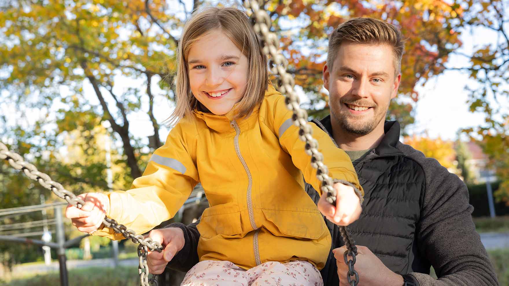 Isä antamassa vauhtia keinussa istuvalle tytölle.