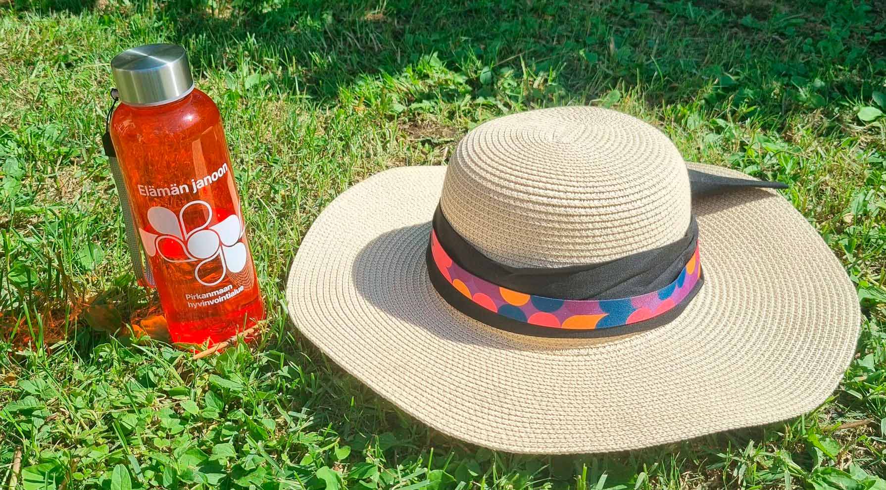 Juomapullo ja hellehattu nurmikolla.