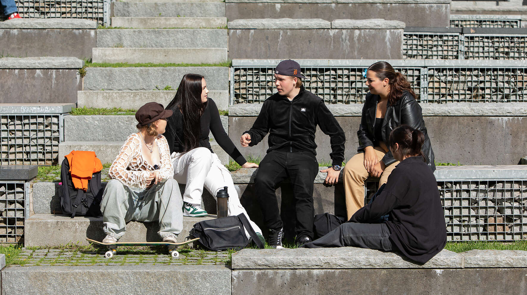 Viisi nuorta istuu rappusilla ja juttelee.