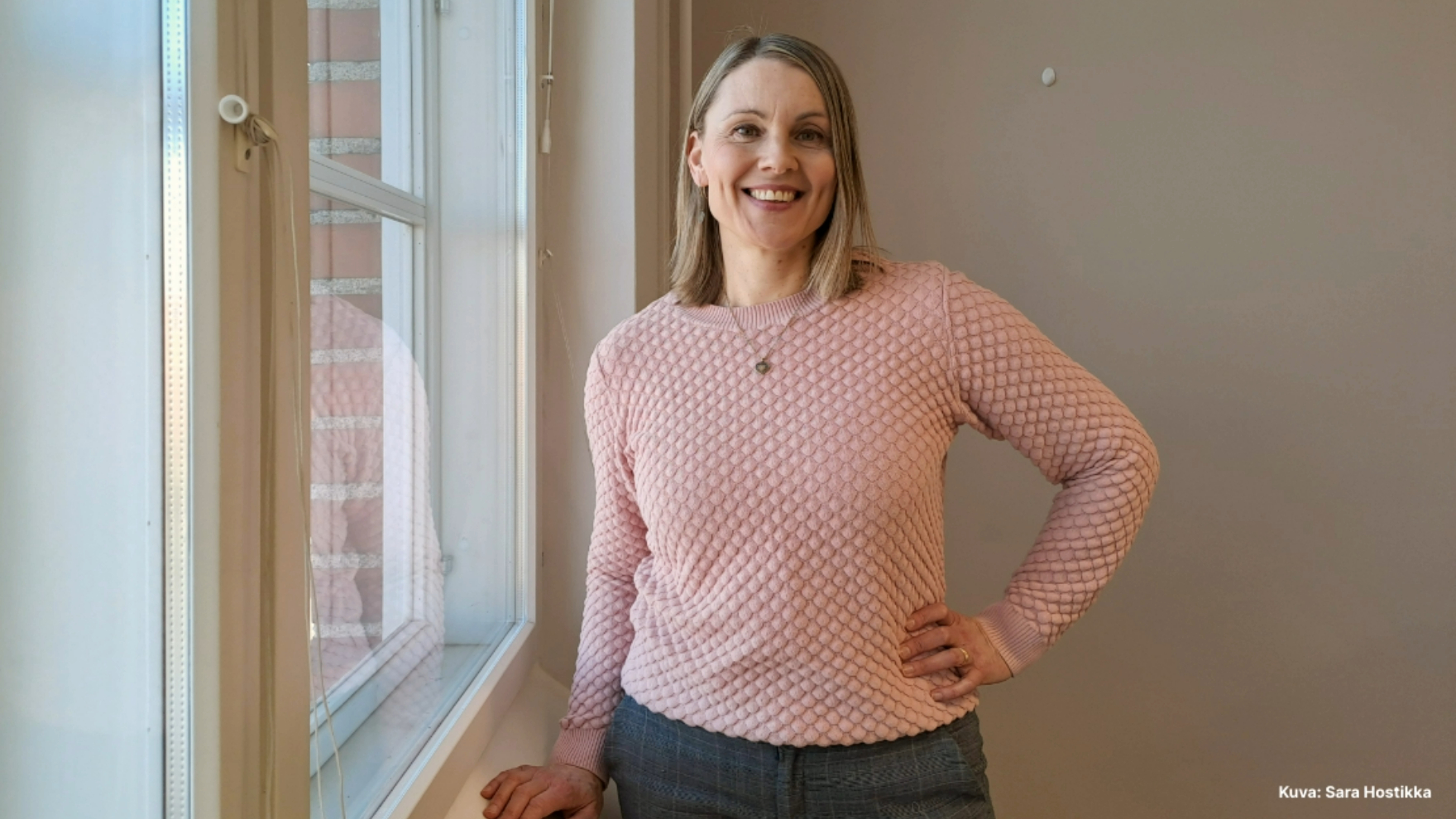 Heli seisoo ikkunan vieressä ja katsoo kameraan.