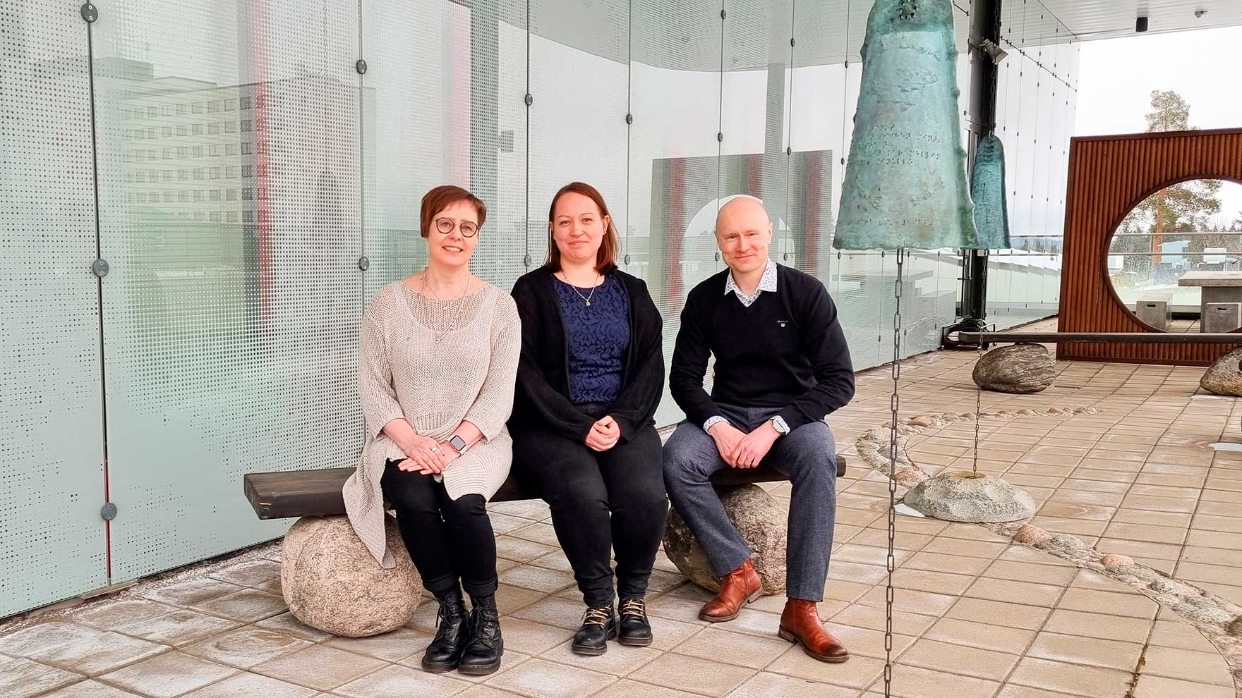 Penkillä istuu kolme hymyilevää henkilöä.