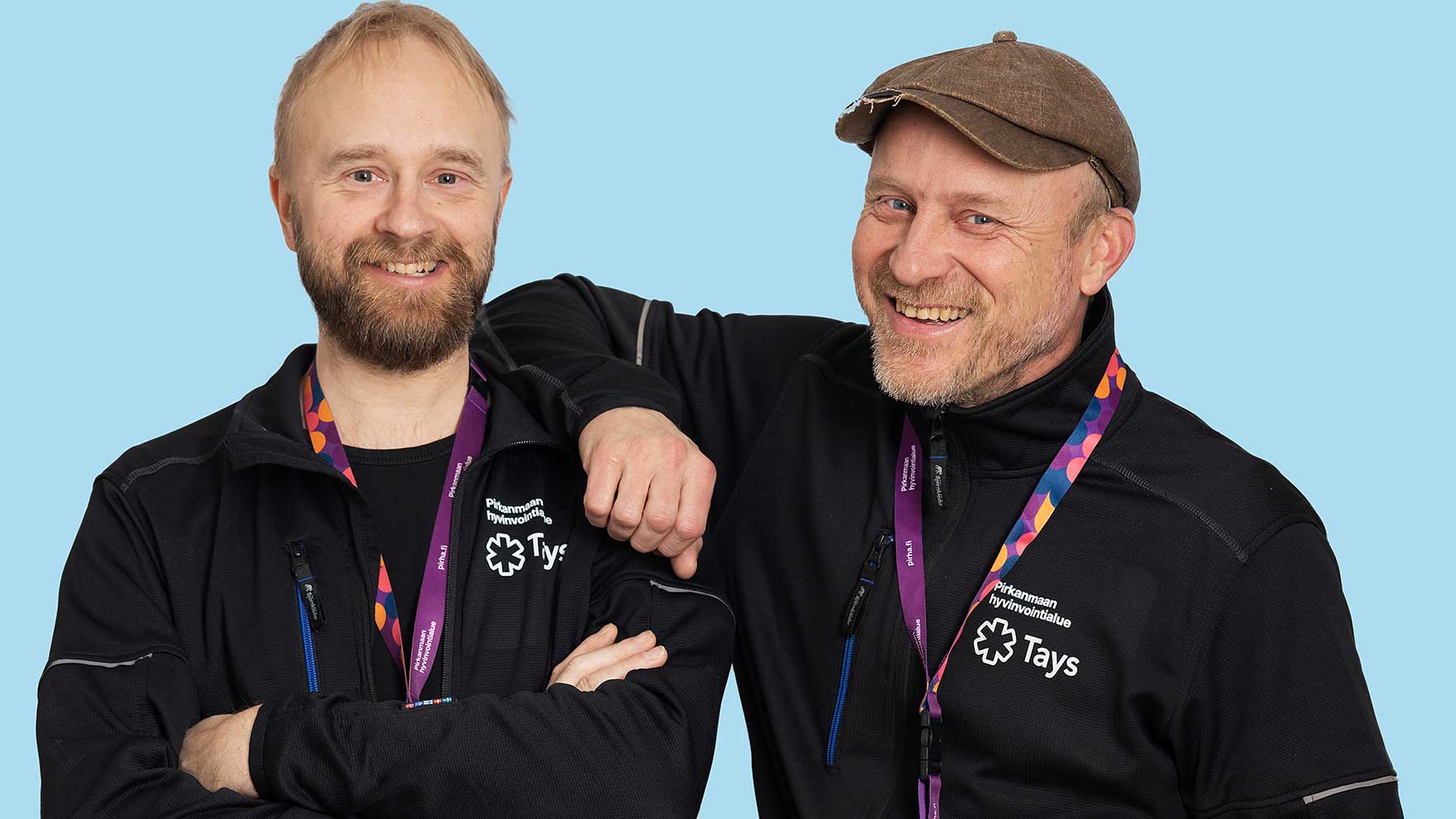 Kaksi parrakasta miestä tummansinissä Taysin takeissa Pirhan henkilökortit kaulassaan. Toisen miehen käsi on toisen olkapäällä.