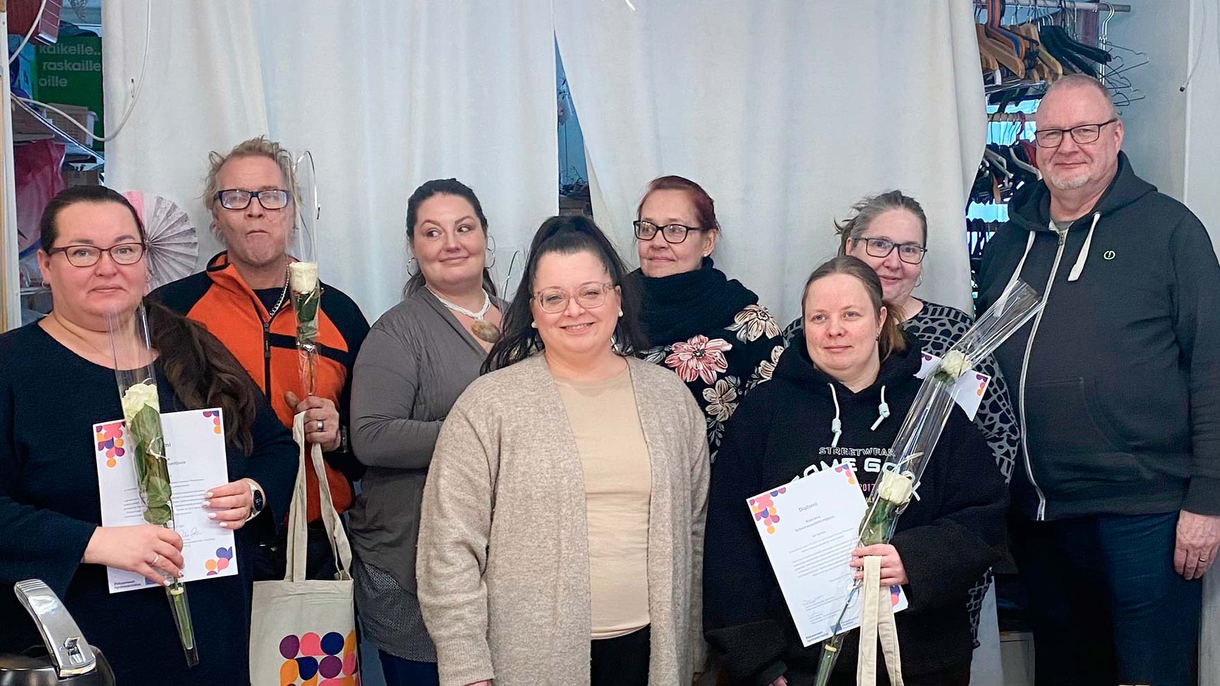 Kahdeksan henkilöä seisoo rinnakkain katsoen kameraan hymyillen. Osalla on kädessään ruusu ja todistus.