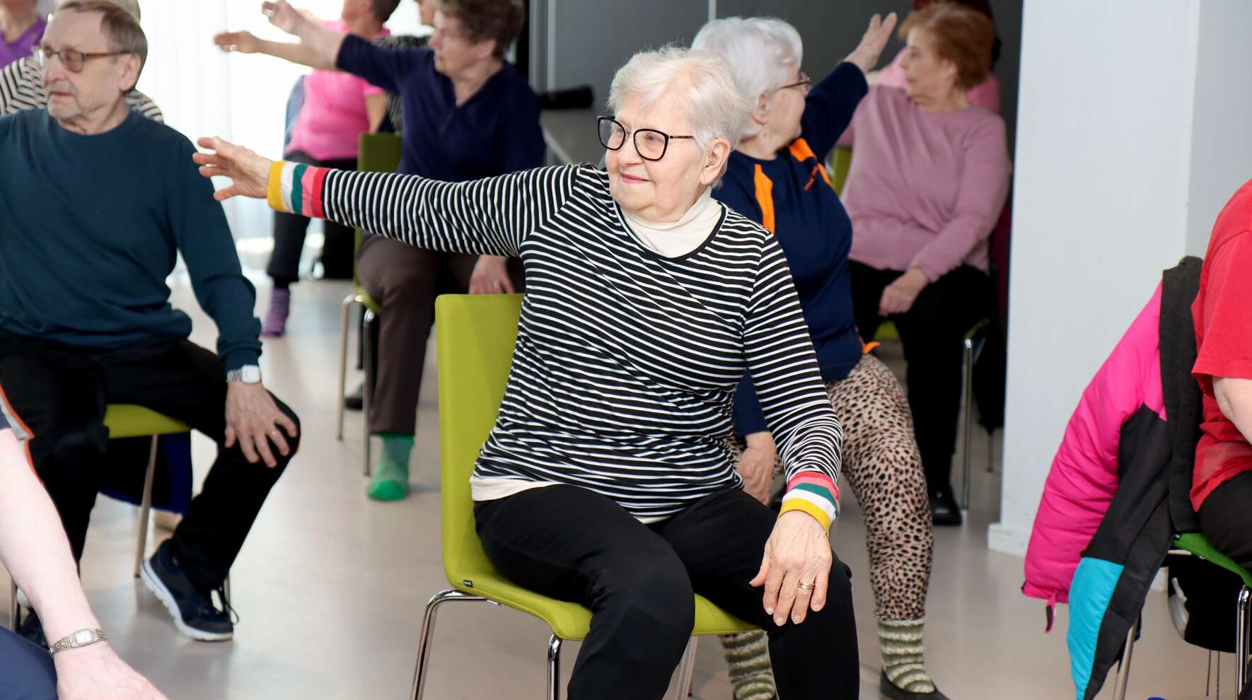 Ikäihmiset venyttävät käsiään penkeillä istuessaan.