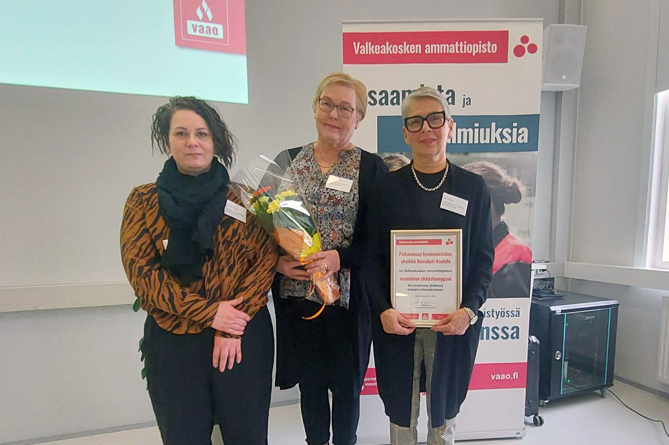Kolme naista seisoo rinnakkain. Keskimmäisellä on kukkakimppu ja oikeanpuoleisella diplomi.