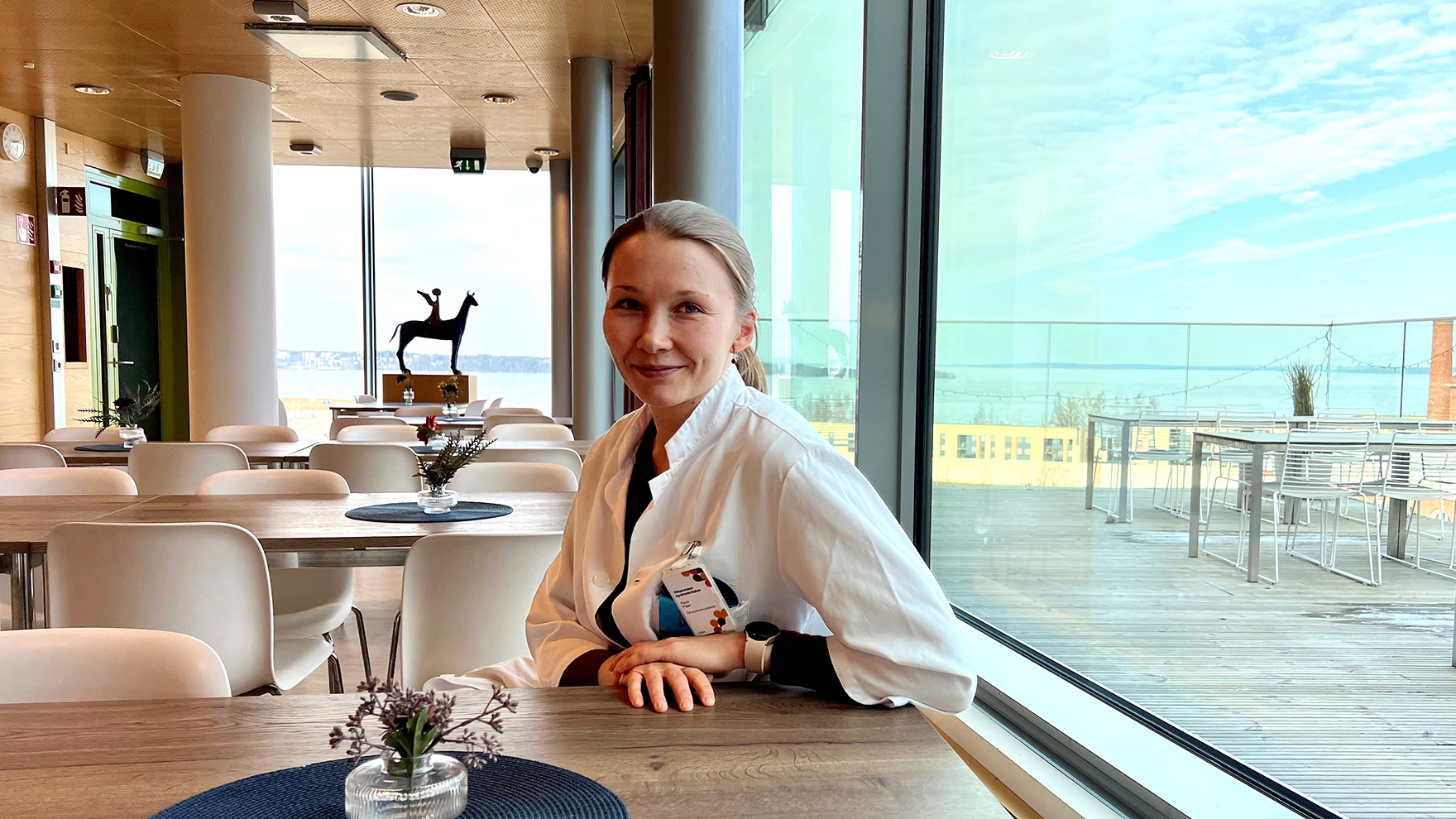 Lääkärintakkiin pukeutunut Paula Pajari istuu kahvilan pöydässä.