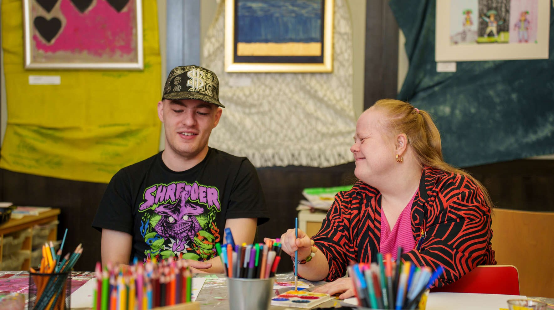 Kehitysvammaiset maalaavat pöydällä, jonka edustalla näkyy värikyniä ja tusseja.