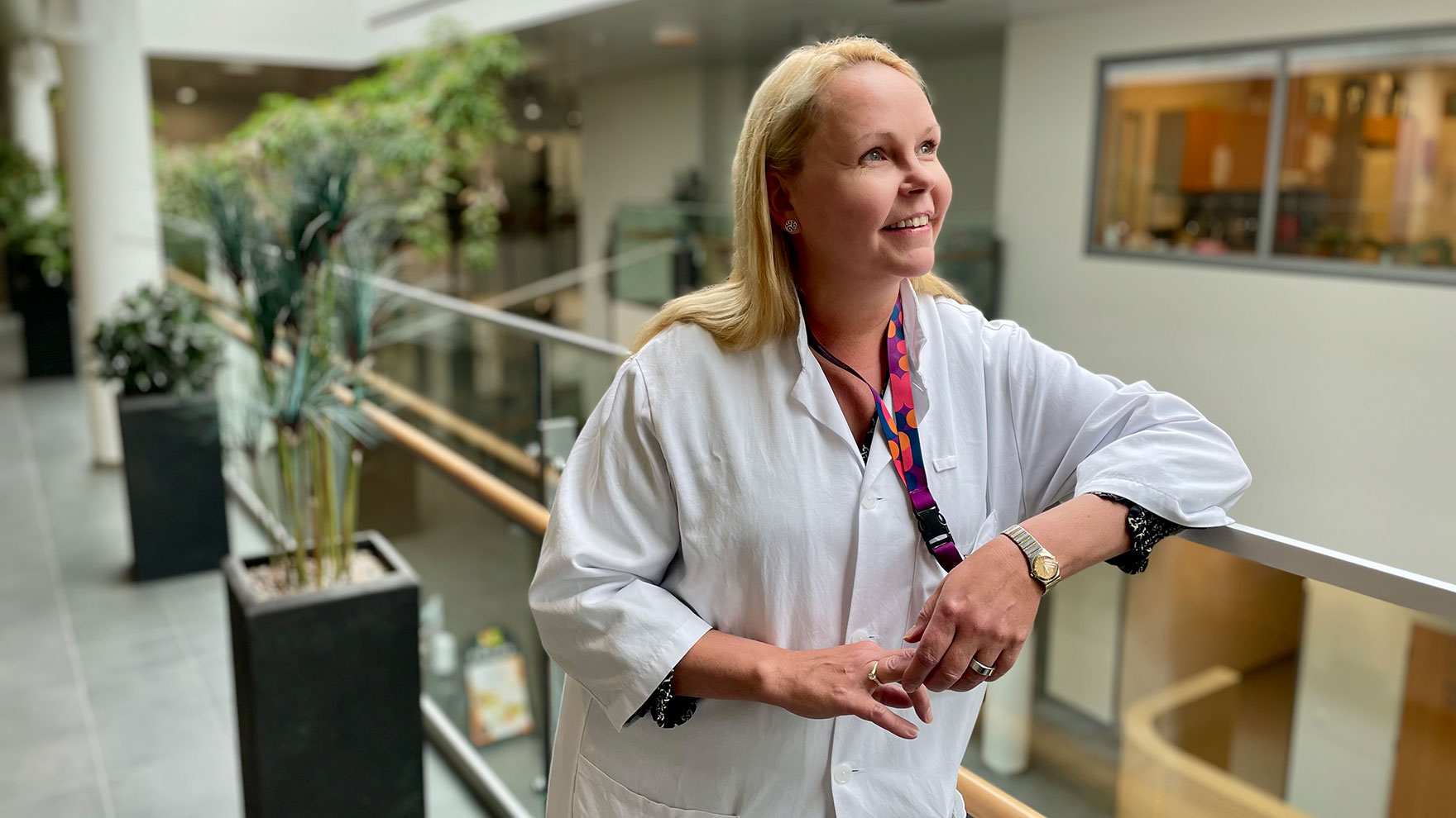Johanna Laukkarinen lääkärintakki yllään nojaa kaiteeseen ja katsoo hymyillen tulevaisuuteen.