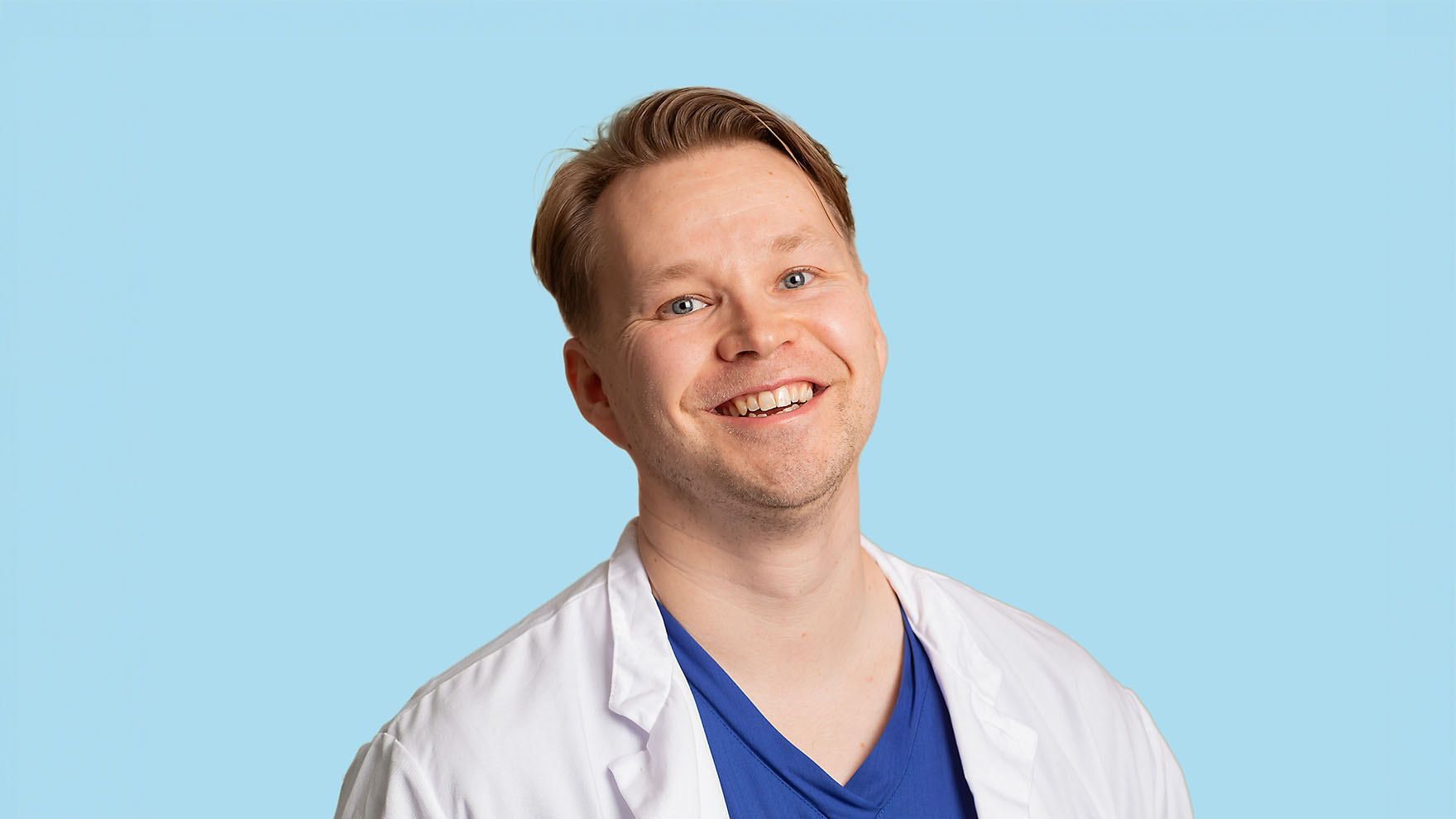 Nuorehko hymyilevä mies, jolla on yllään sininen paita ja valkoinen takki.