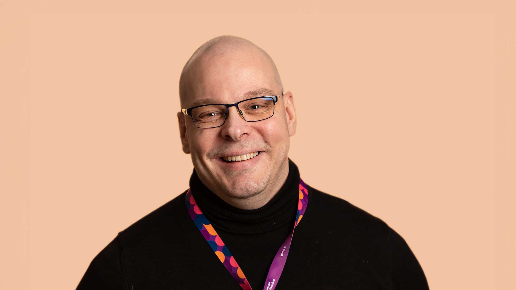 Hymyilevä silmälasipäinen mies, jolla on tumma poolopusero ja kaulassa värikäs avainnauha.