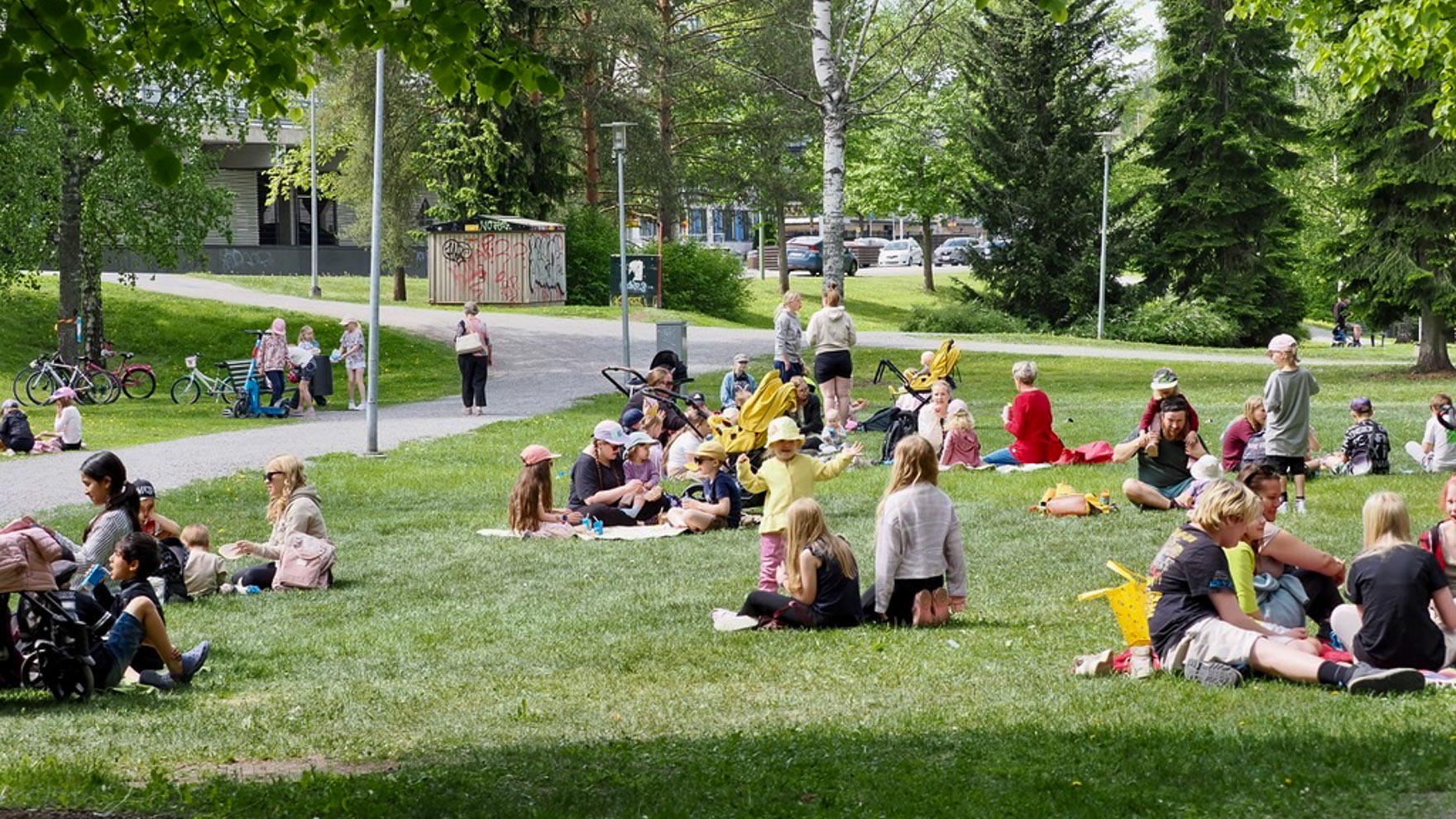 Ihmisiä istuu pienissä porukoissa puistossa syömässä puistoruokaa.