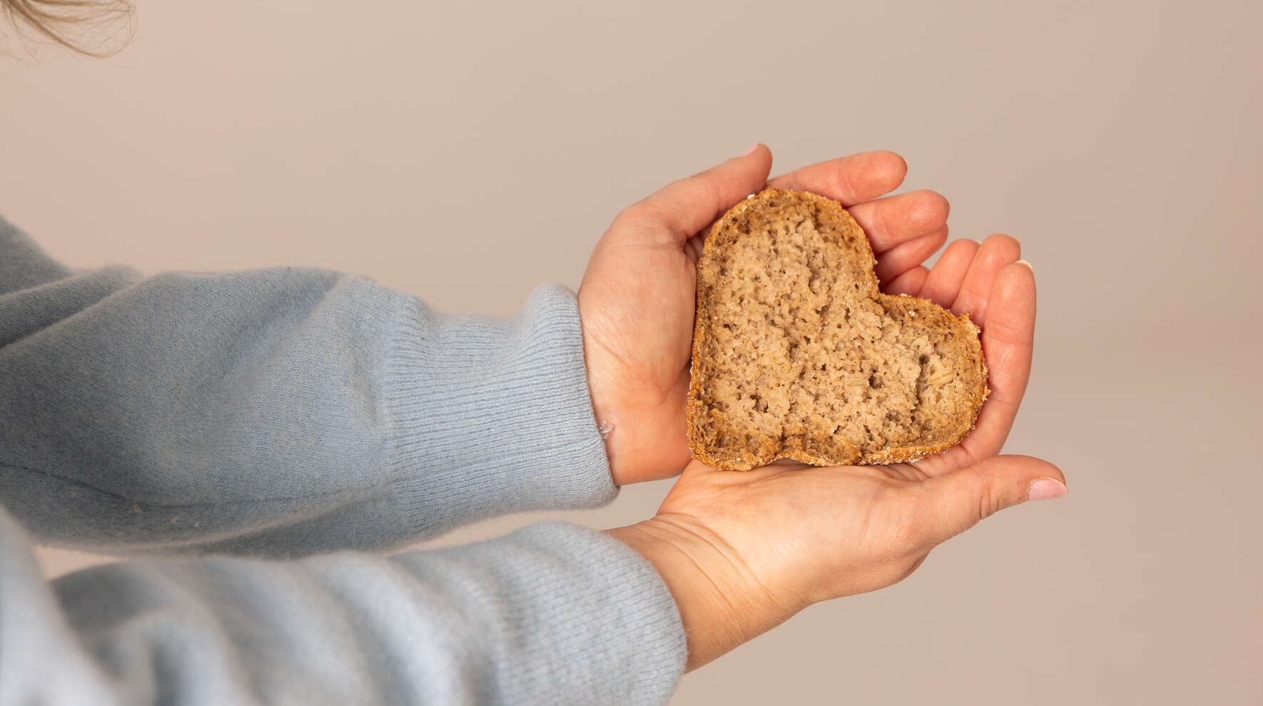 Kädet, jotka pitelevät sydämen muotoista leipää.