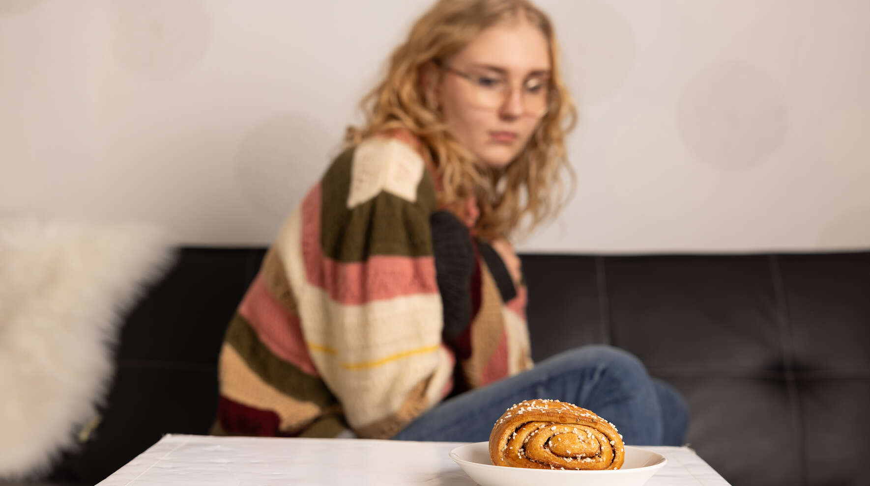 Tyttö istuu sohvalla ja katsoo empien sohvapöydällä lautasella olevaa korvapuustia.