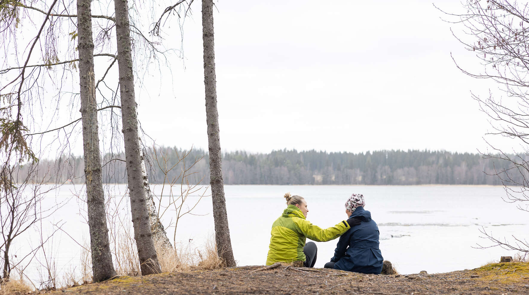Kaksi henkilöä rannalla istumassa, toisen käsi toisen olkapäällä.