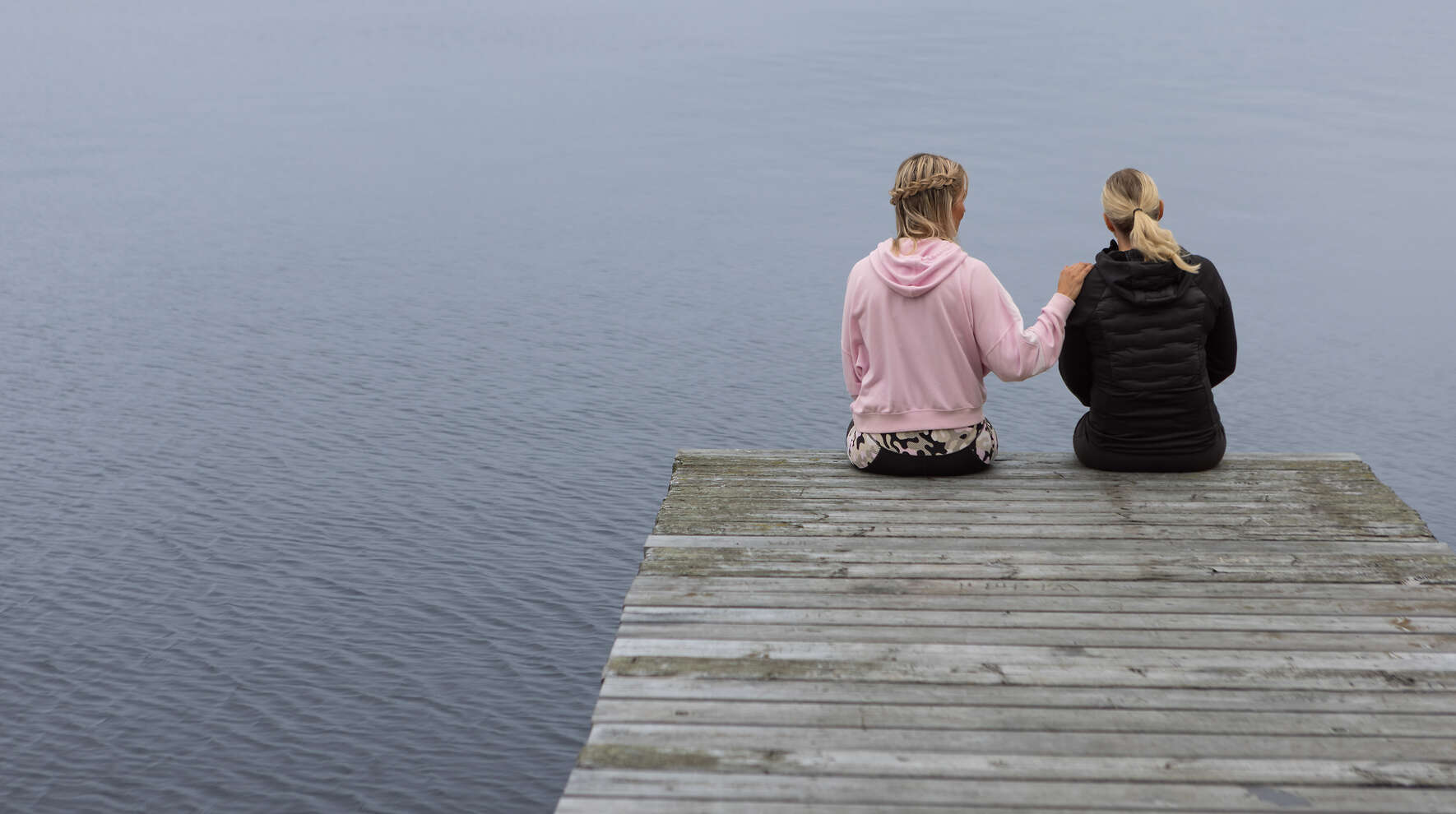 Käsi toisen olkapäällä laiturilla istuessa.