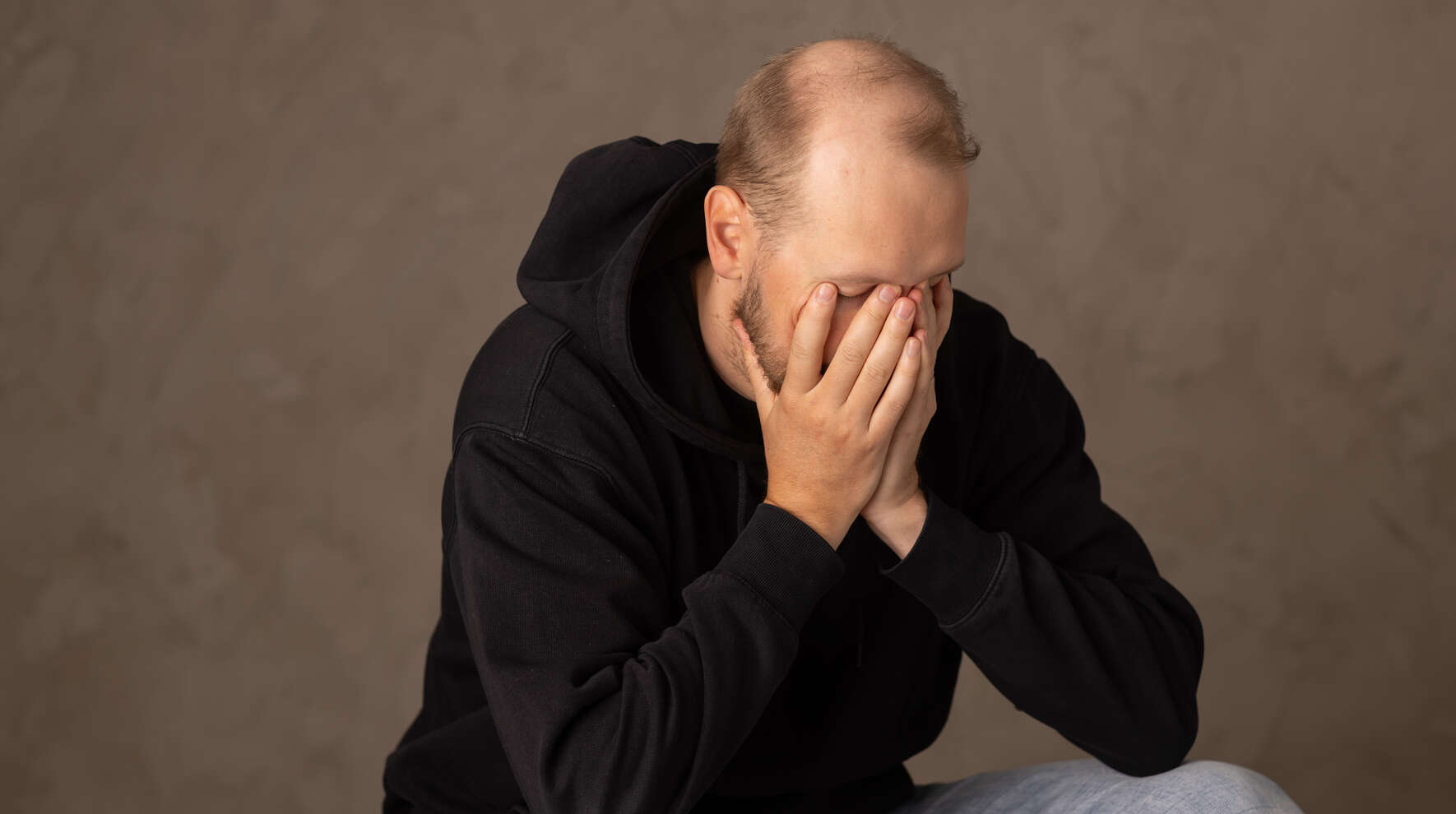 Mies istuu kädet kasvoillaan.