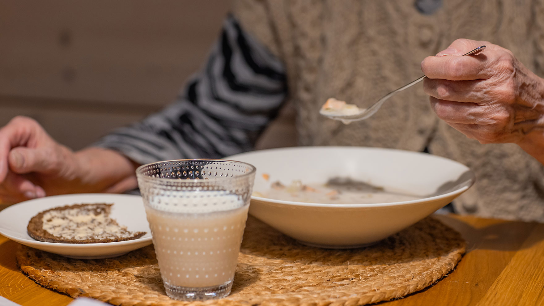 Ikäihminen syömässä keittoa, ruisleipää ja maitoa.