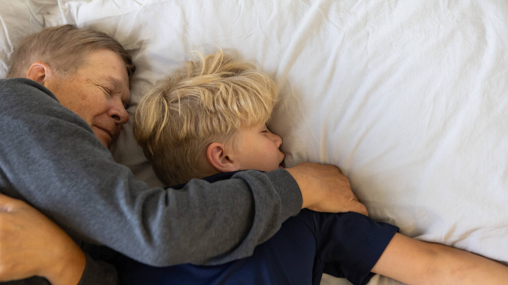 Vanhempi mies ja pieni poika makaavat silmän kiinni sängyllä, miehen käsi on pojan hartialla.