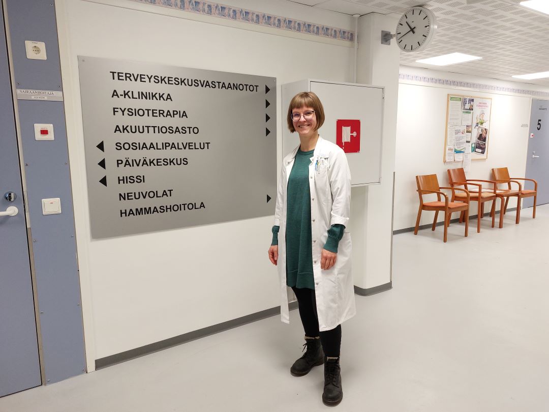 Nainen hymyilee käytävälle seisten.