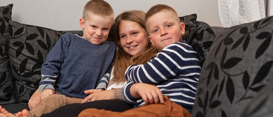 Tyttö ja kaksi poikaa istuu tiiviinä rykelmänä sohvalla.