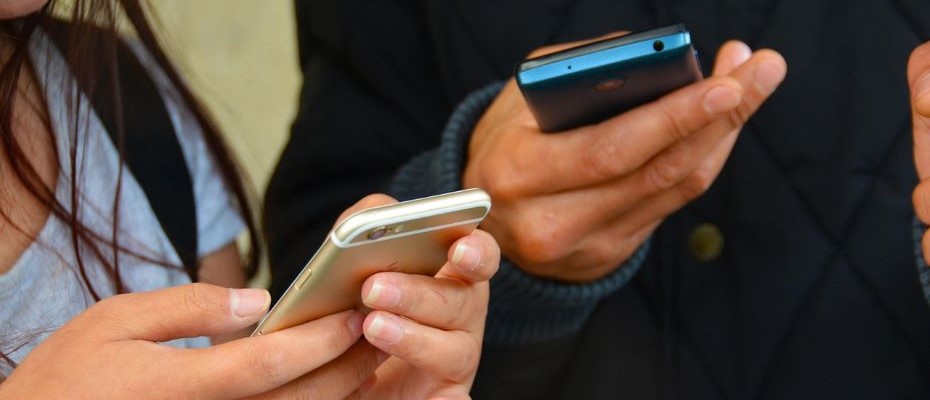 Kaksi henkilöä seisoo vierekkäin. Molemmilla on mobiililaitteet käsissään.