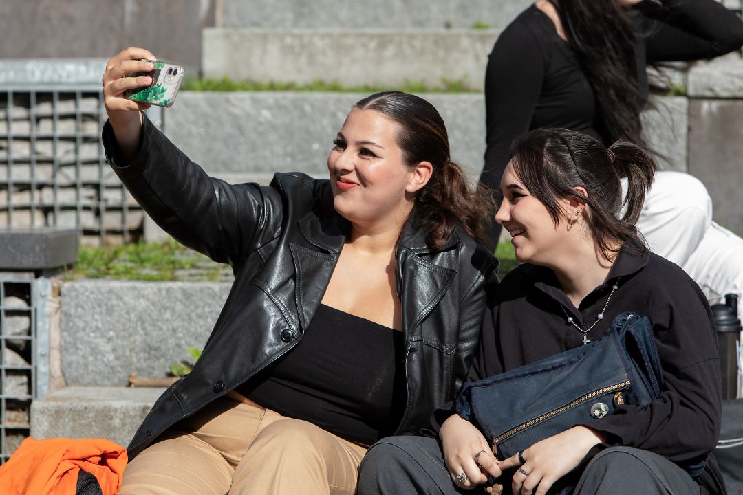 Kaksi naista istuu vierekkäin ja ottaa kuvaa puhelimella itsestään.