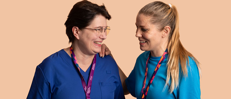 Two employees of the Wellbeing services county of Pirkanmaa stand next to each other smiling.