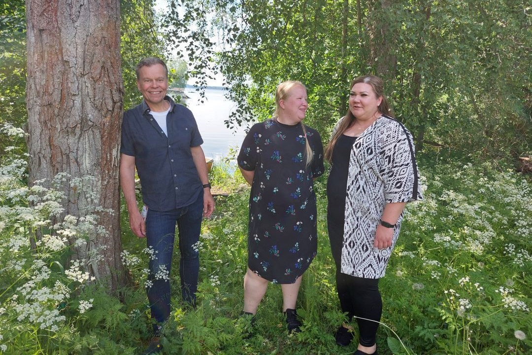 Kaksi naista ja yksi mies seisoo järven rannalla.
