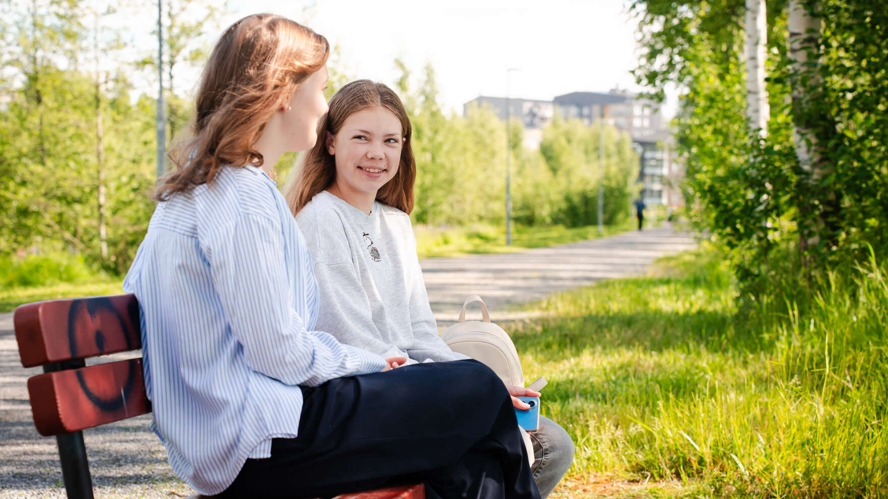 Kaksi nuorta juttelemassa ulkona puistonpenkillä.