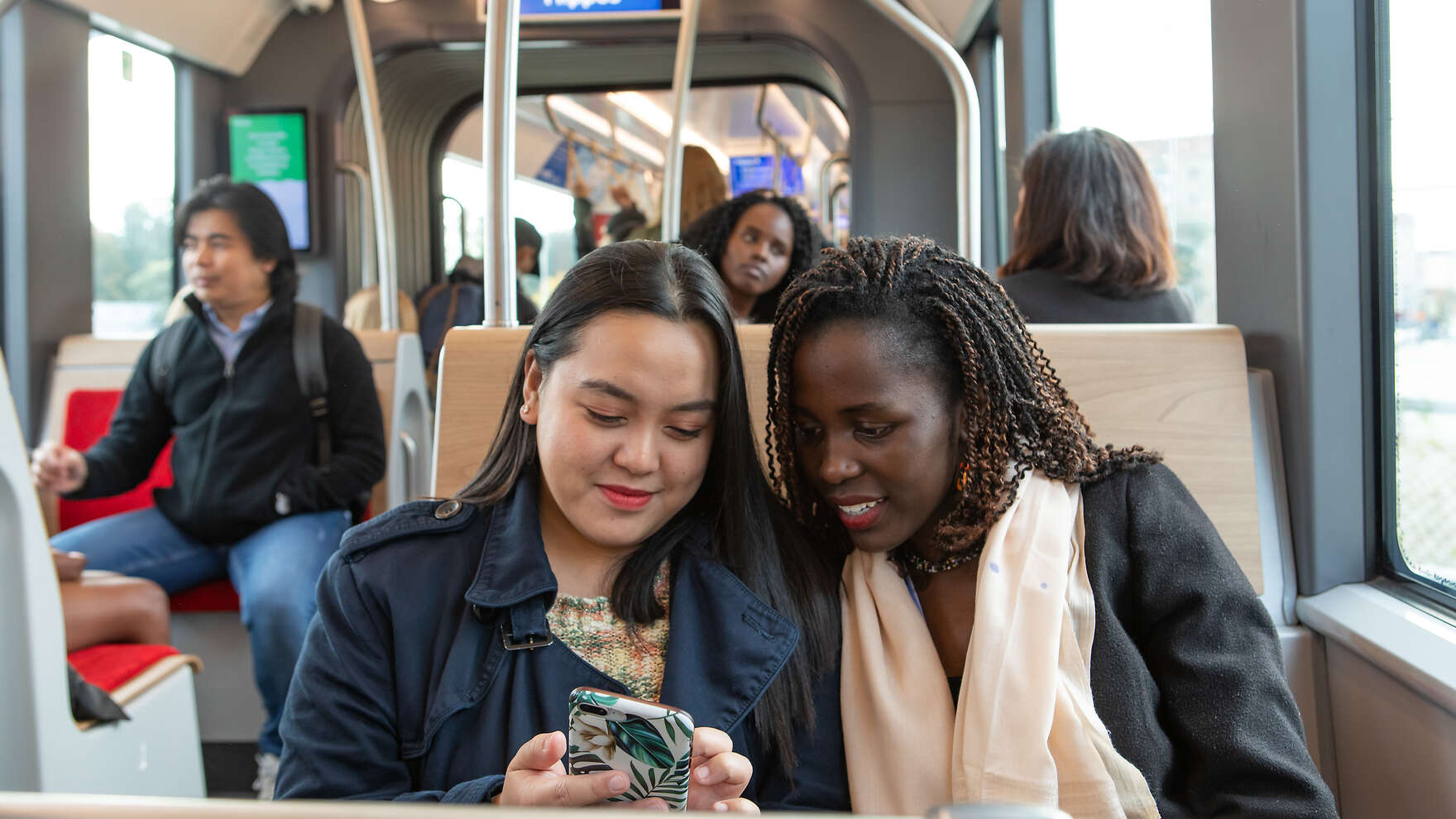 Two women are sitting on a tram and looking at a mobile phone.