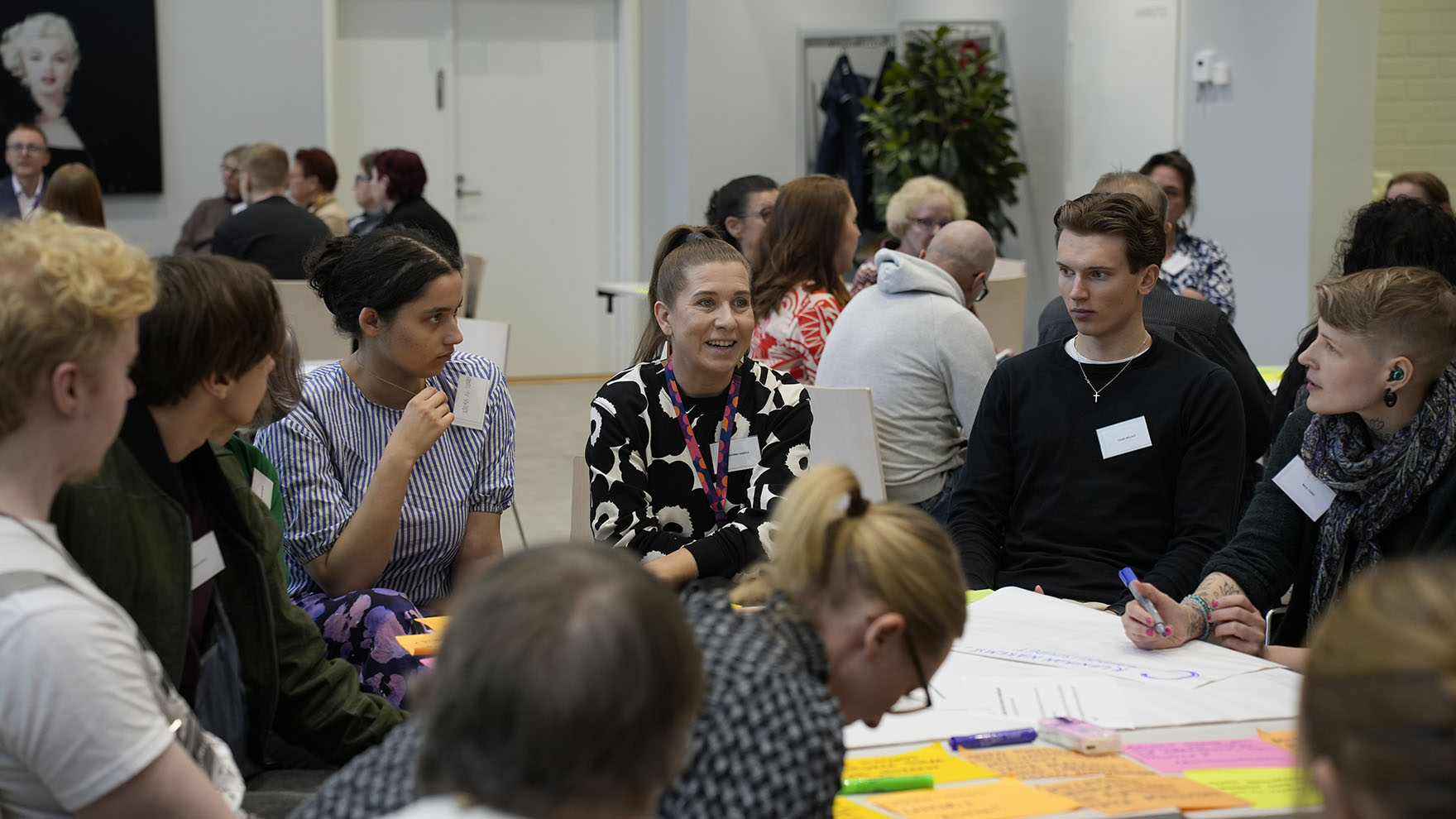 Asukaspaneelin osallistujia salissa istumassa ryhmissä ja keskustelemassa.