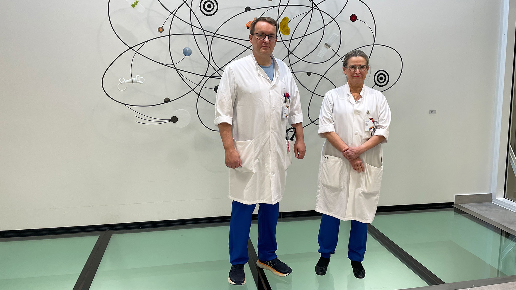 Valokuva Jaana Syrjäsestä ja Petrus Säilästä infektioyksikön taideteoksen edessä.