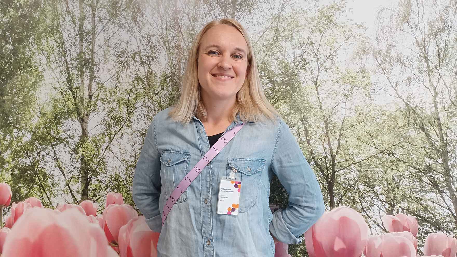 Heli Kalliomäki hymyilee kameralle luontoaiheisen valokuvaseinän edessä.