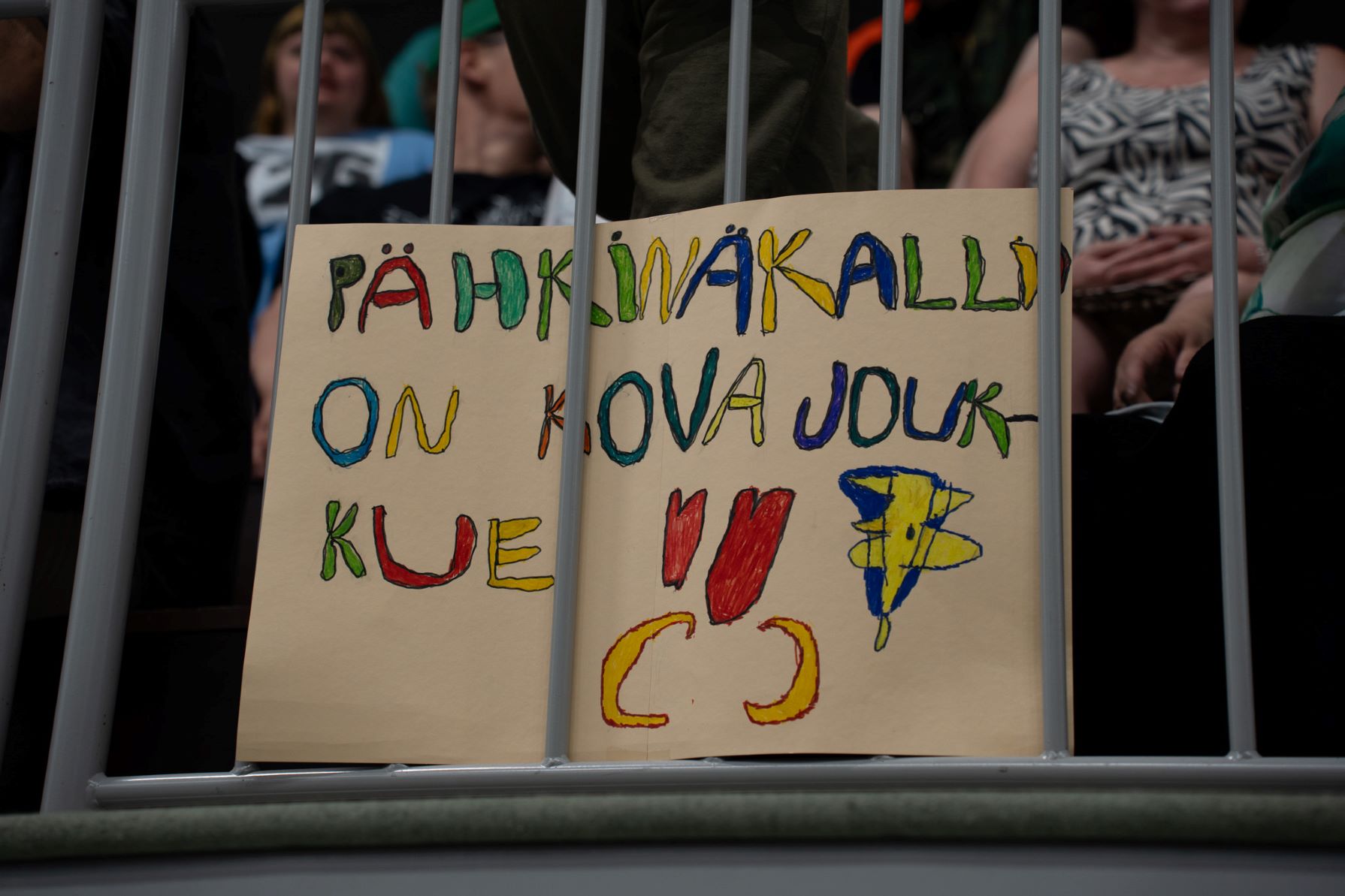 Katsojien joukossa banneri, jossa on värikästä tekstiä.