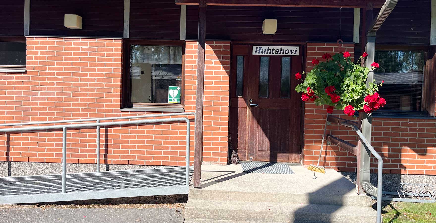 Punatiilisen talon sisäänkäynti, jonne on pyörätuoliramppi. Oven yläpuolella lukee Huhtahovi.