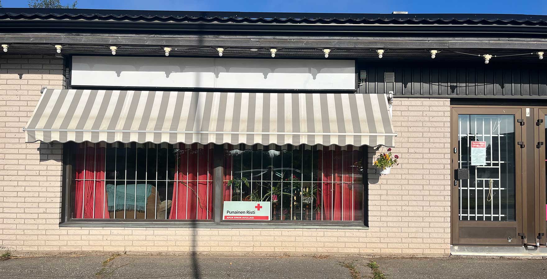 Keltainen tillirakennus, jonka yhdessä ikkunassa Punaisen ristin tunnus.
