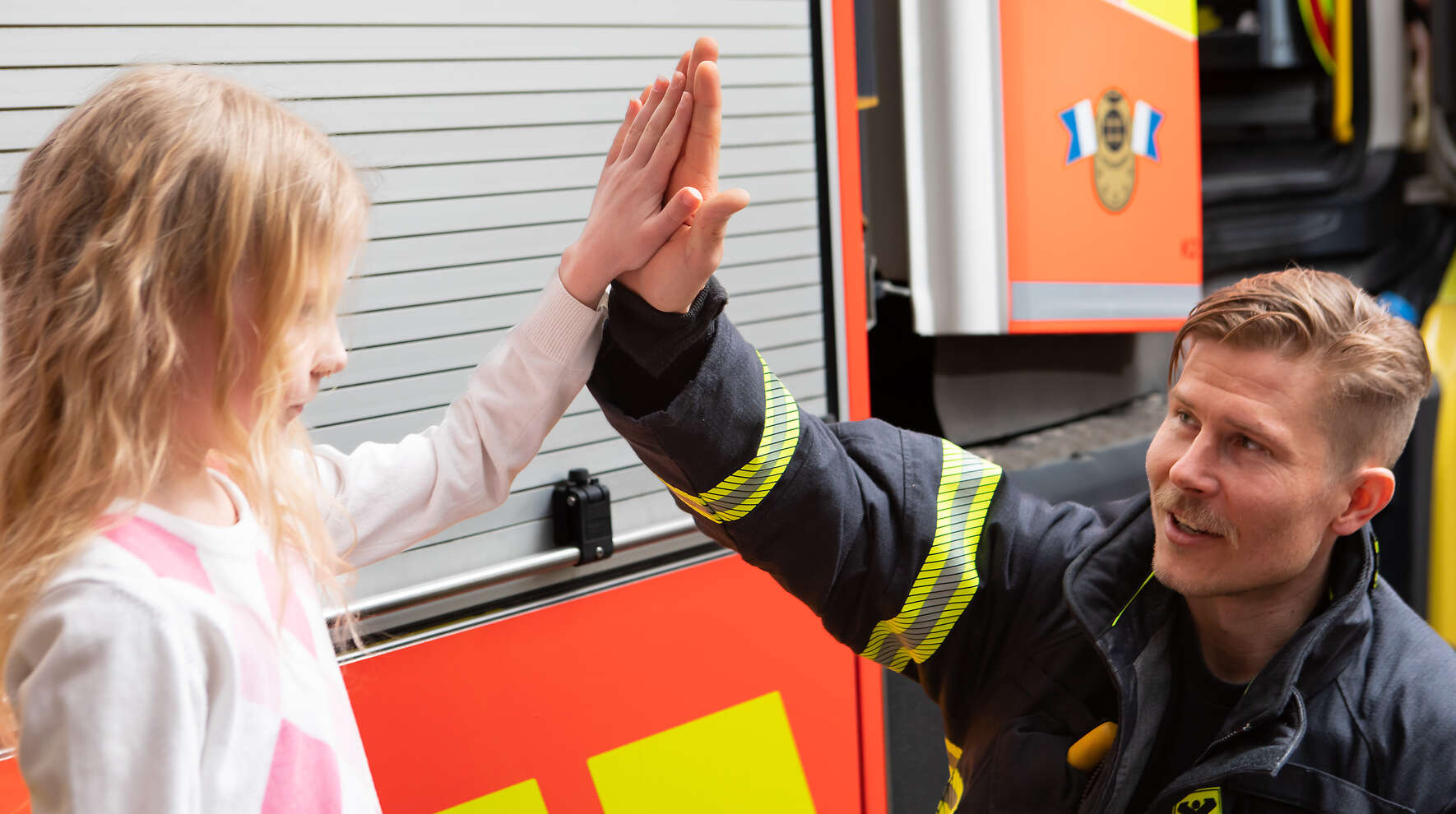 Kuvassa lapsi ja pelastaja kohtaavat paloauton vierellä.