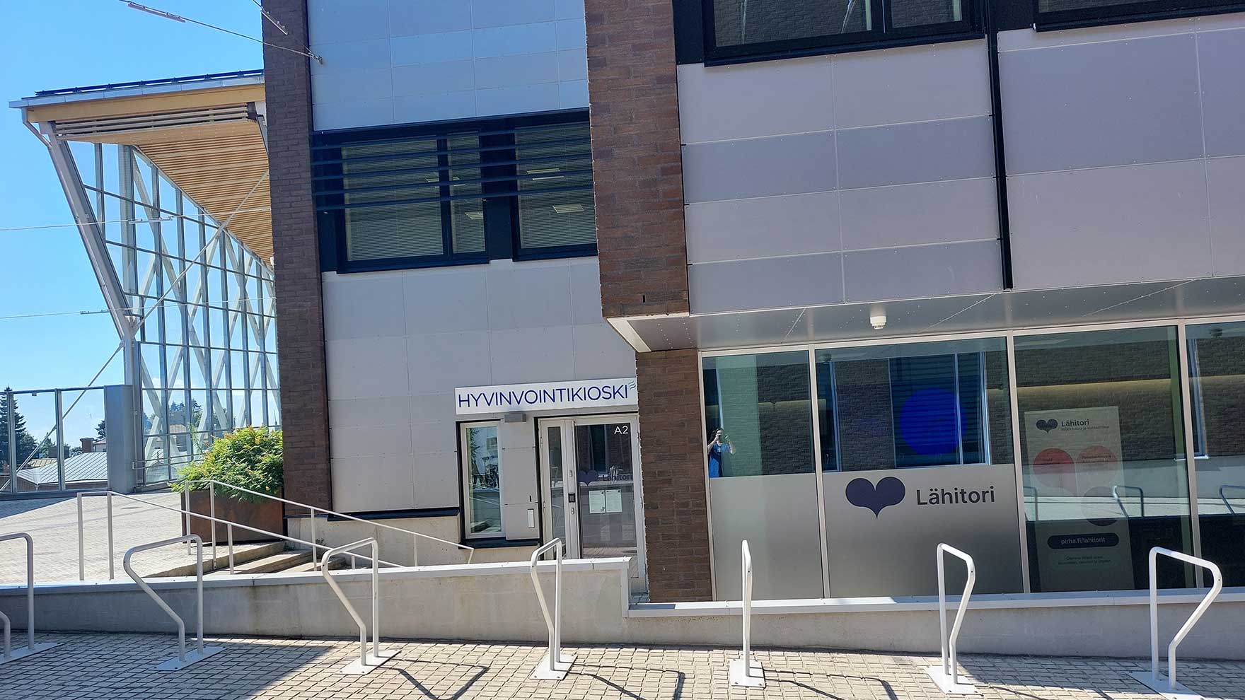 Hyvinvointikioskin sisäänkäynti, jonka viereisessä ikkunassa on lähitorin tunnus.