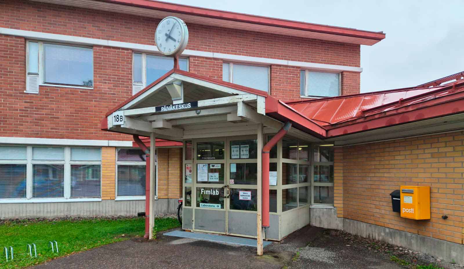 Sisäänkäynti puna-keltatiiliseen rakennukseen, oven yläpuolella lukee Päiväkeskus.