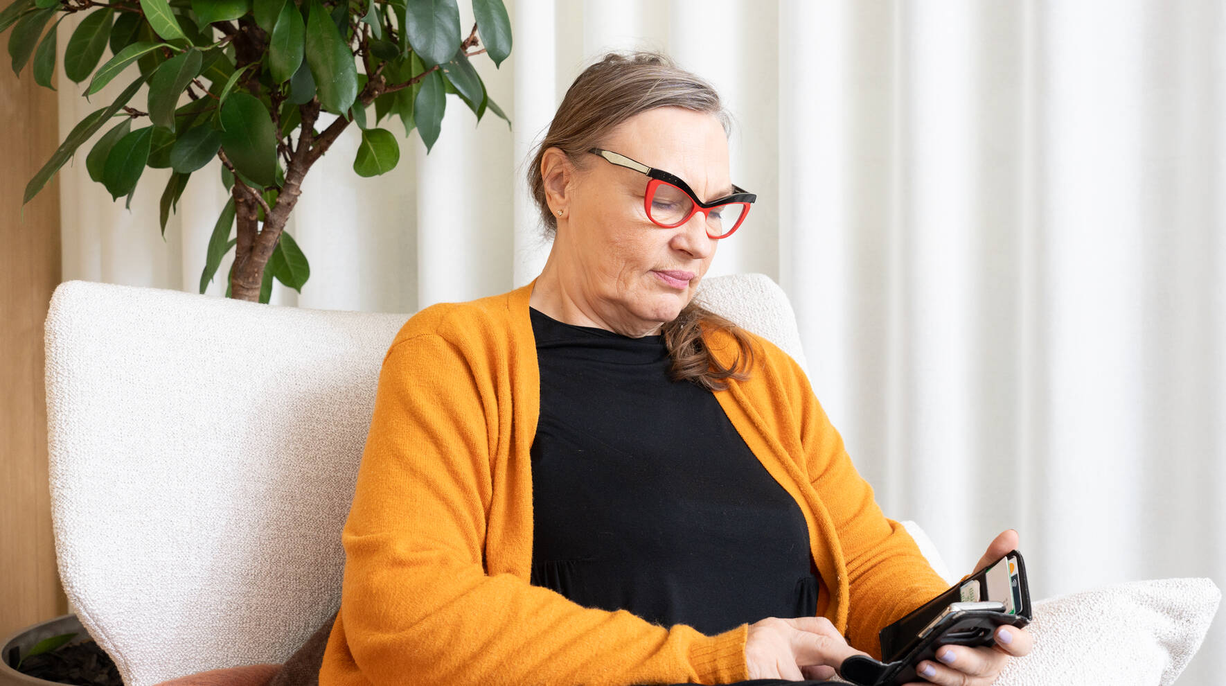 Nainen istuu tuolissa ja näppäilee puhelinta.